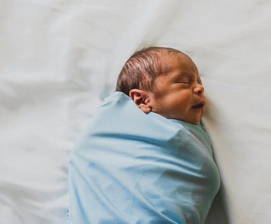 Newborn baby wrapped in blue swaddle sleeping peacefully