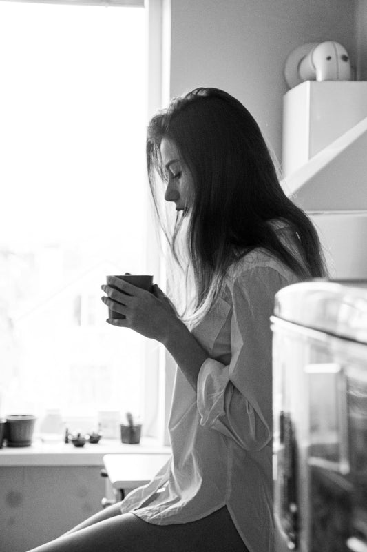 A mother holding a cup of coffee, looking reflective by a window