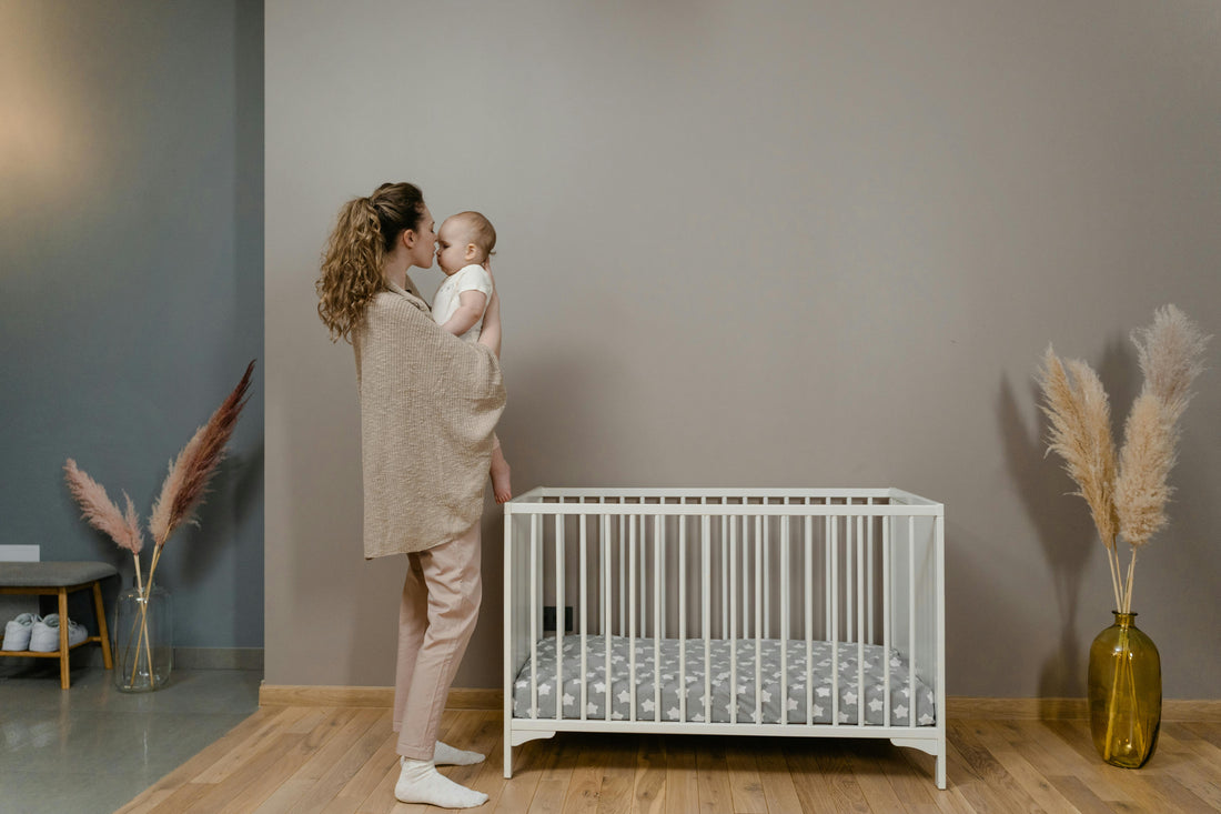 Mother holding baby close in a calm nursery next to a white cot