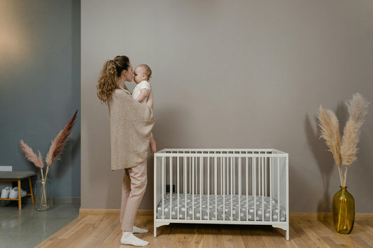 Mother holding baby close in a calm nursery next to a white cot