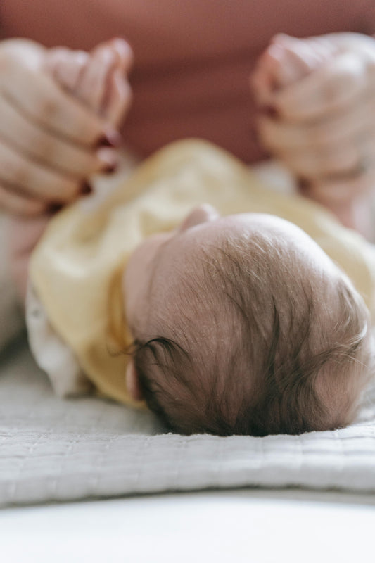 Newborn baby lying on a soft white surface with parent's hands nearby