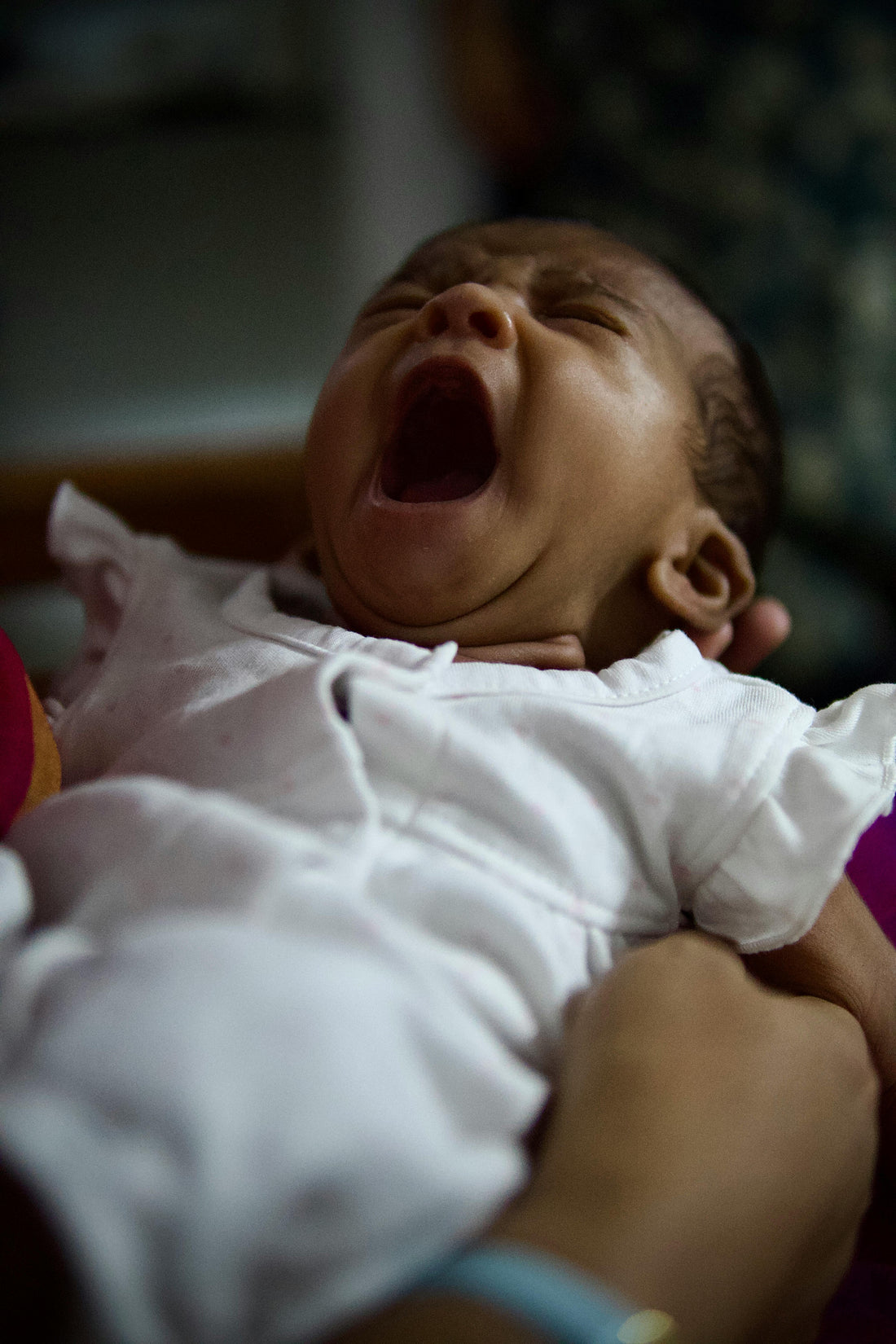 Newborn baby crying loudly while being held by a parent