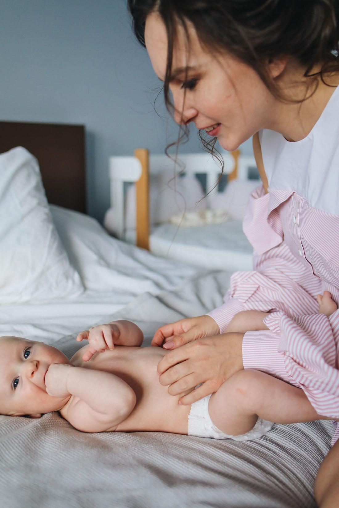 Mother smiling at her baby lying on a bed